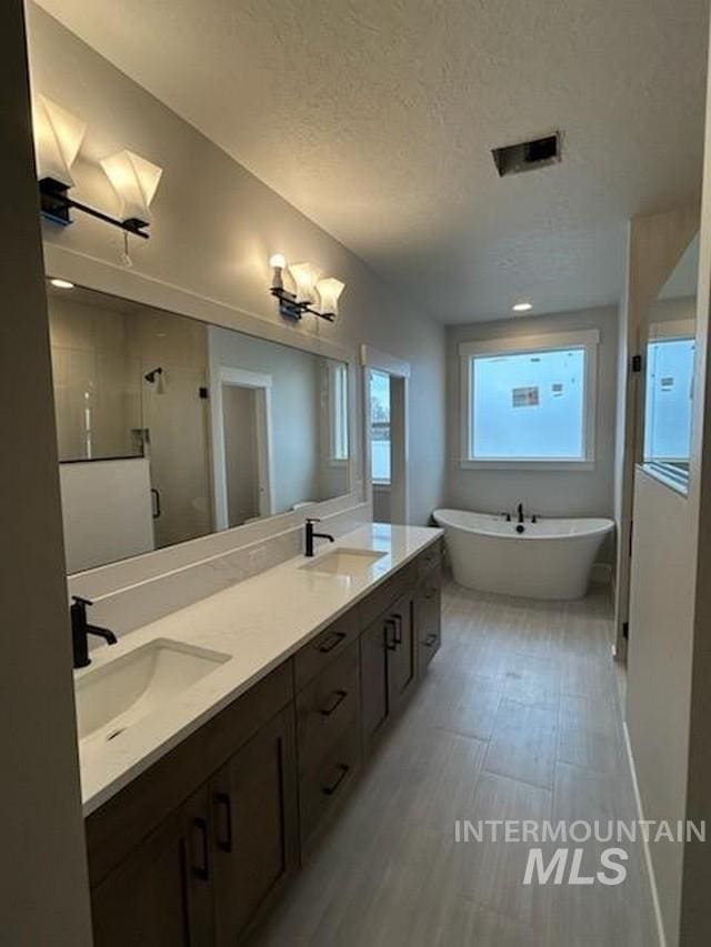 full bathroom featuring a textured ceiling, a sink, a soaking tub, a shower stall, and double vanity