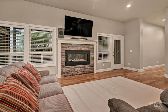 living area featuring a stone fireplace, recessed lighting, wood finished floors, and baseboards