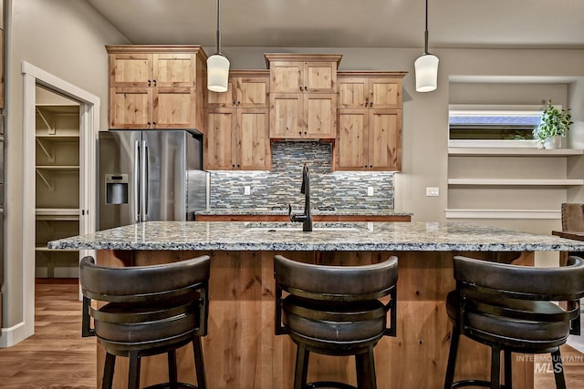 kitchen with light stone counters, stainless steel fridge, tasteful backsplash, and wood finished floors