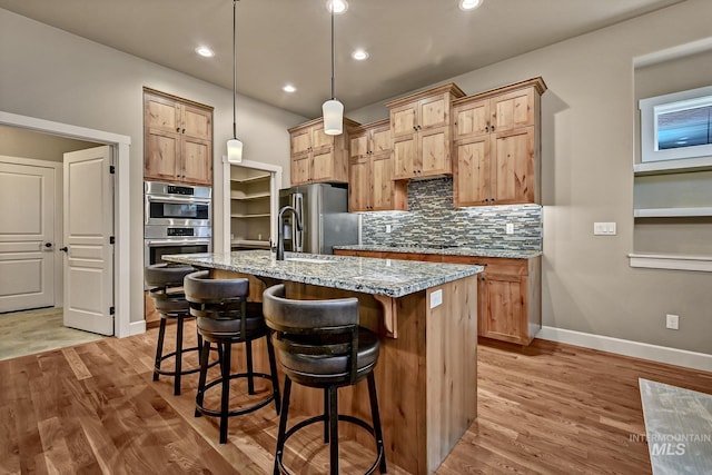 kitchen featuring backsplash, light stone countertops, a breakfast bar area, appliances with stainless steel finishes, and light wood-style floors