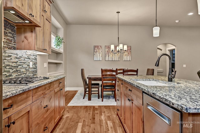 kitchen featuring a sink, light stone counters, backsplash, light wood-style floors, and appliances with stainless steel finishes