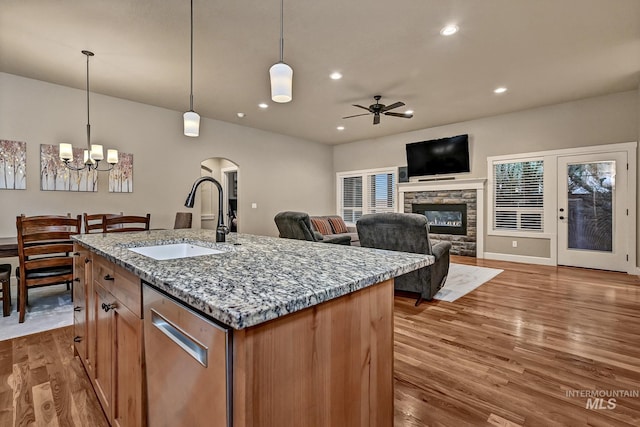 kitchen with a sink, wood finished floors, recessed lighting, a stone fireplace, and light stone countertops