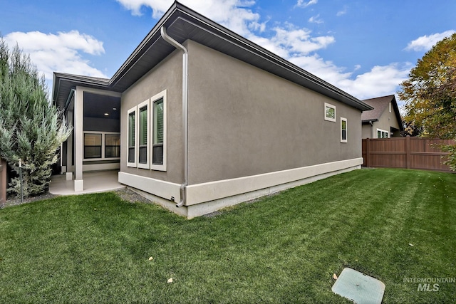 view of side of property featuring a patio, a yard, fence, and stucco siding