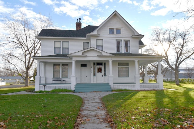 victorian home with covered porch, a chimney, and a front yard