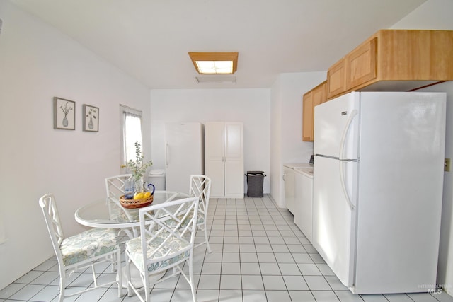 kitchen with light tile patterned floors, washer / clothes dryer, light brown cabinetry, and freestanding refrigerator