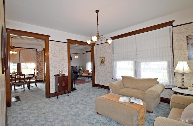 carpeted living area featuring wallpapered walls, baseboards, and ceiling fan with notable chandelier