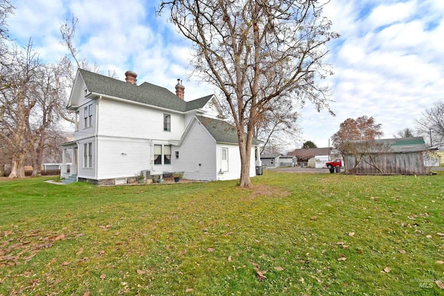 rear view of house with entry steps, a yard, and a chimney