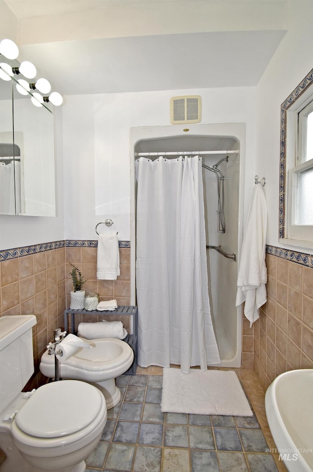 bathroom featuring a stall shower, visible vents, toilet, a wainscoted wall, and tile walls