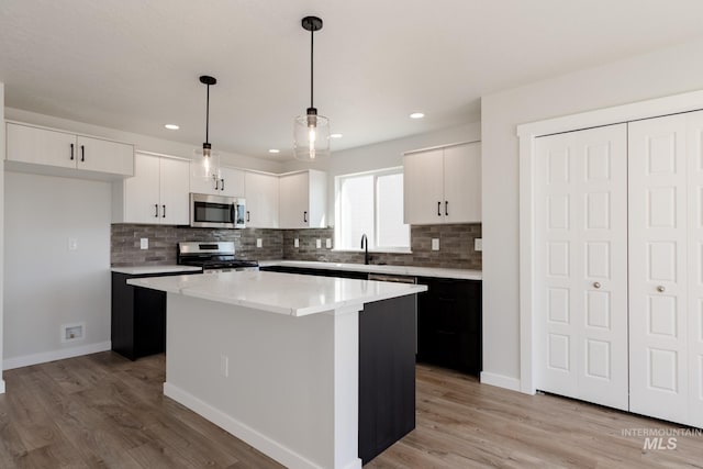 kitchen featuring a center island, stainless steel appliances, light wood-style floors, white cabinetry, and a sink