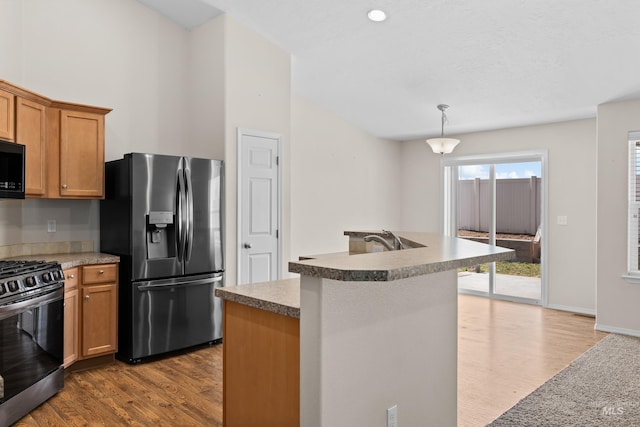 kitchen featuring wood finished floors, a kitchen island with sink, appliances with stainless steel finishes, pendant lighting, and brown cabinets