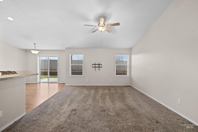 unfurnished living room featuring light carpet, ceiling fan, and baseboards