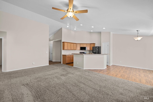 kitchen featuring stainless steel microwave, a kitchen island, open floor plan, light countertops, and black fridge