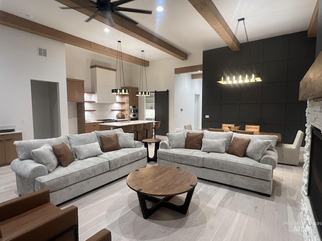 living area with a stone fireplace, a barn door, a ceiling fan, light wood finished floors, and beamed ceiling