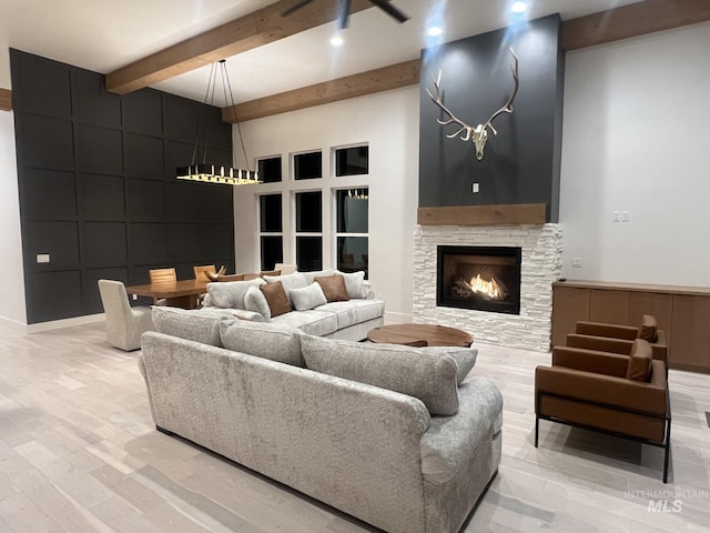 living room featuring a fireplace, light wood finished floors, a decorative wall, a towering ceiling, and beamed ceiling