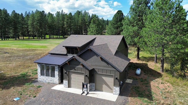 view of front of property featuring stone siding, driveway, board and batten siding, a front lawn, and a standing seam roof