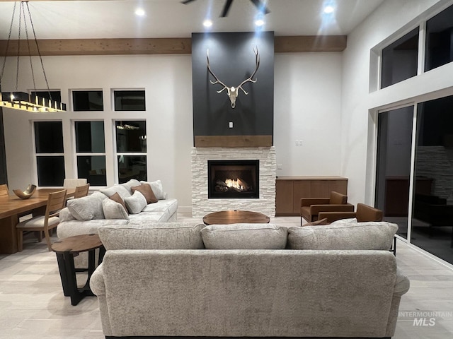 living area featuring a towering ceiling, light wood-style floors, beam ceiling, and a stone fireplace