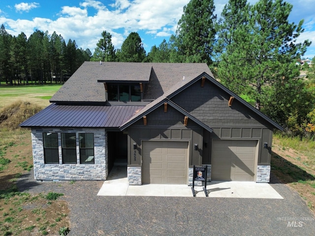 view of front of property featuring metal roof, aphalt driveway, an attached garage, stone siding, and board and batten siding