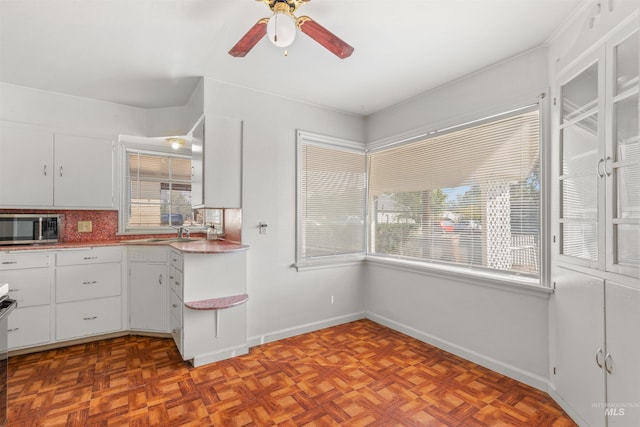 kitchen with decorative backsplash, light parquet floors, white cabinets, and ceiling fan