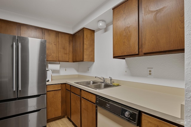 kitchen with a sink, freestanding refrigerator, brown cabinetry, light countertops, and white dishwasher