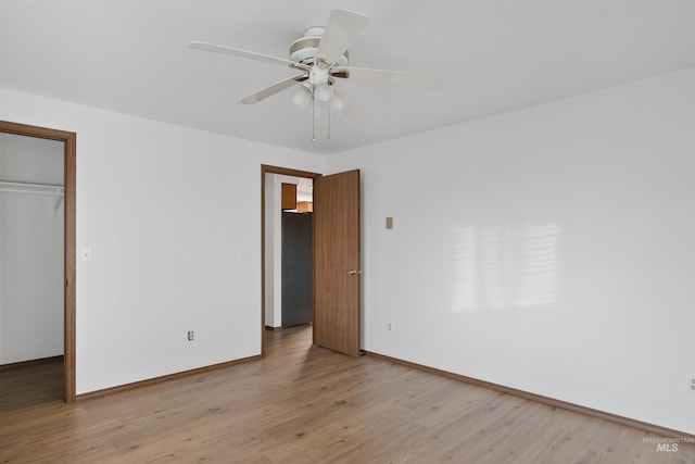 unfurnished bedroom featuring black refrigerator, light wood-style flooring, baseboards, and a closet