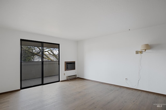 empty room with an AC wall unit, wood finished floors, baseboards, and a baseboard radiator