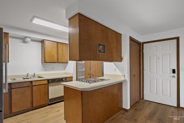 kitchen featuring brown cabinets, a sink, a peninsula, stainless steel cooktop, and dishwashing machine