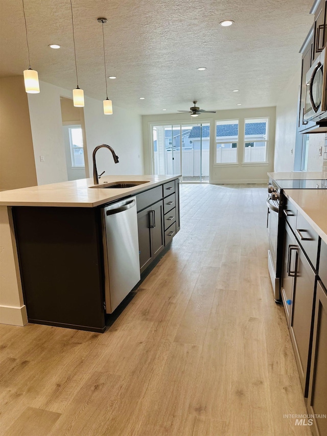 kitchen with pendant lighting, sink, a textured ceiling, appliances with stainless steel finishes, and an island with sink