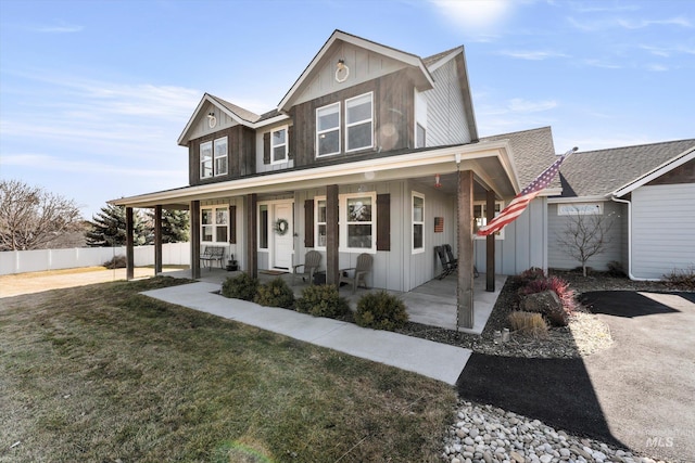 view of front of house with covered porch, a front lawn, board and batten siding, and fence