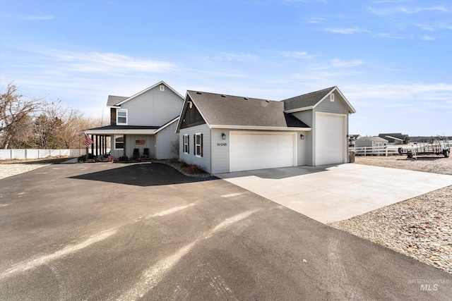 view of front of house with driveway, roof with shingles, an attached garage, and fence