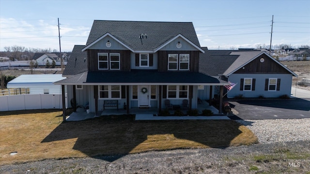 view of front facade with a front lawn, fence, a porch, and a shingled roof