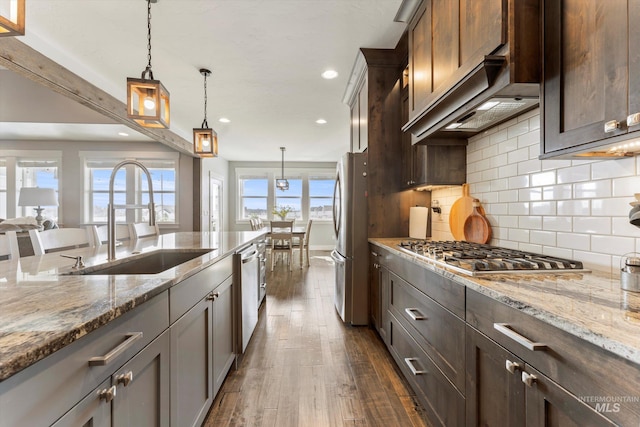 kitchen with light stone counters, stainless steel appliances, dark wood-style flooring, a sink, and decorative backsplash