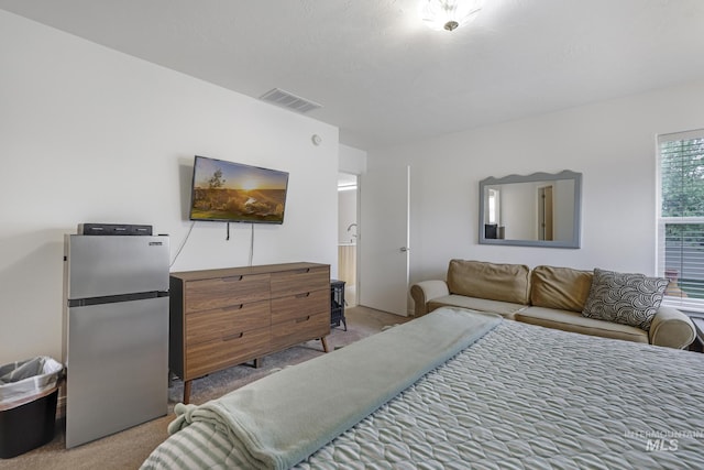 bedroom featuring visible vents, freestanding refrigerator, and light carpet