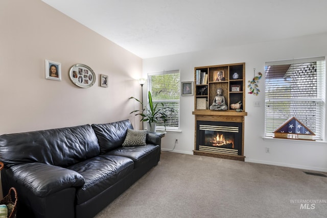 living room featuring visible vents, vaulted ceiling, baseboards, a glass covered fireplace, and carpet