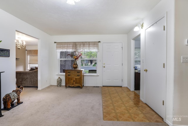 entryway with an inviting chandelier, baseboards, and light colored carpet