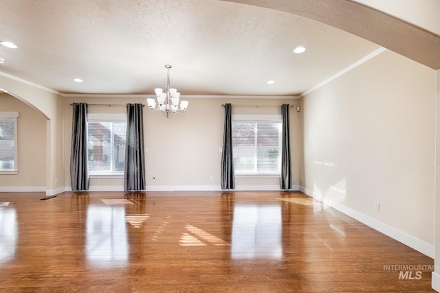 empty room featuring ornamental molding, wood finished floors, arched walkways, and a healthy amount of sunlight