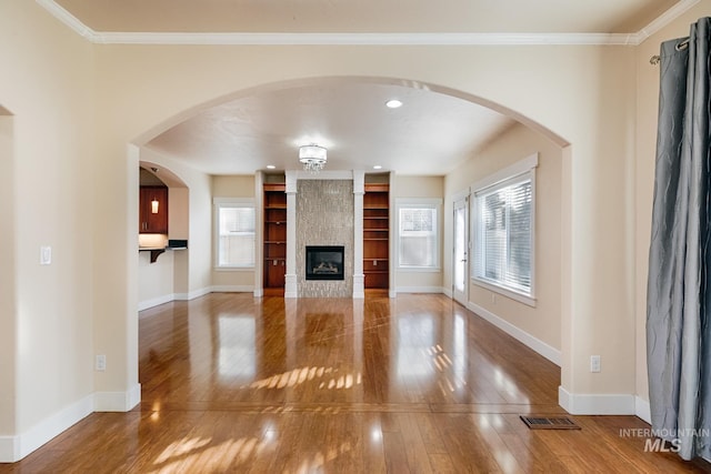 unfurnished living room featuring visible vents, hardwood / wood-style flooring, crown molding, a fireplace, and baseboards