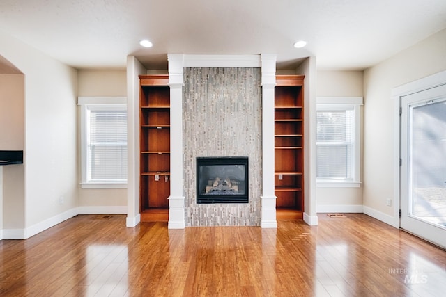 unfurnished living room with wood finished floors, visible vents, baseboards, recessed lighting, and a glass covered fireplace