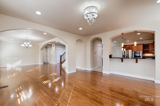 unfurnished living room featuring a notable chandelier, light wood-style floors, recessed lighting, and baseboards