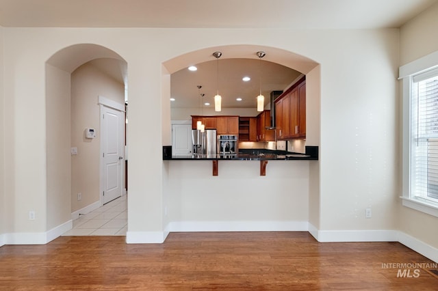 kitchen featuring dark countertops, light wood finished floors, a breakfast bar area, brown cabinets, and appliances with stainless steel finishes