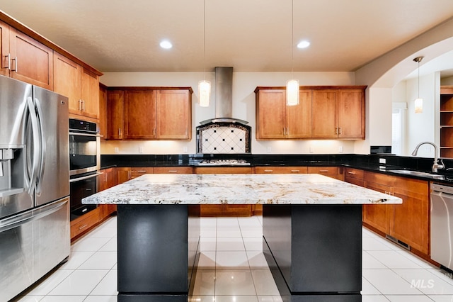 kitchen with a sink, stainless steel appliances, wall chimney exhaust hood, brown cabinets, and a center island