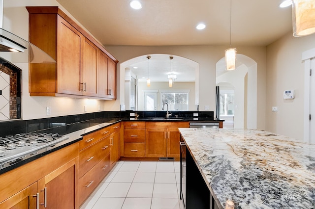 kitchen featuring light tile patterned floors, light stone counters, brown cabinetry, gas stovetop, and a sink