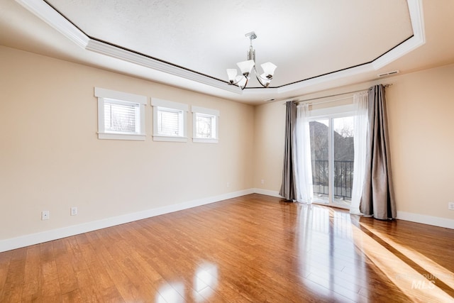 empty room featuring light wood finished floors, visible vents, baseboards, a chandelier, and a raised ceiling