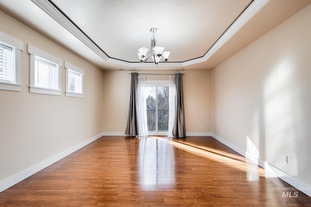 unfurnished room with crown molding, baseboards, a chandelier, a tray ceiling, and wood finished floors