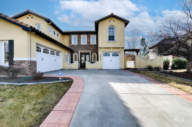 mediterranean / spanish-style home with a gate, an attached garage, stucco siding, concrete driveway, and stone siding