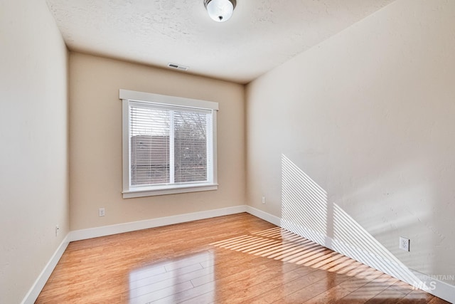 spare room with visible vents, baseboards, a textured ceiling, and wood finished floors