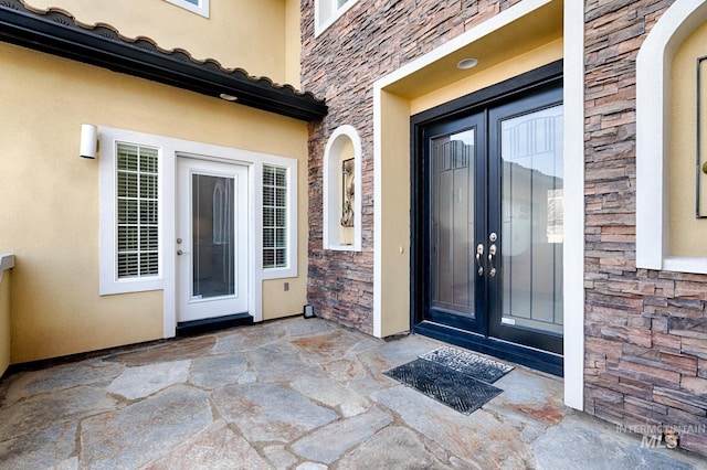 view of exterior entry featuring a tiled roof, stone siding, stucco siding, and french doors