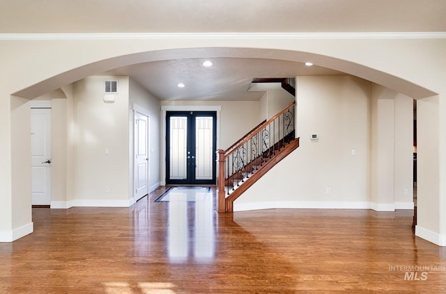 foyer entrance with arched walkways, french doors, baseboards, and wood finished floors