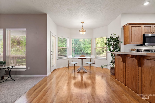 kitchen featuring stainless steel microwave, baseboards, light countertops, brown cabinetry, and light wood-type flooring