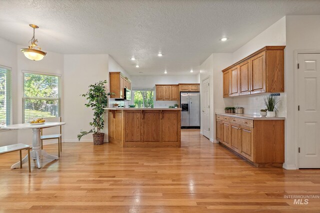 kitchen featuring stainless steel fridge with ice dispenser, a peninsula, light wood-style floors, brown cabinetry, and a textured ceiling