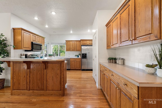 kitchen with stainless steel appliances, a peninsula, light wood-style floors, brown cabinets, and a kitchen bar